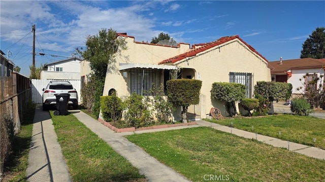 view of front facade with a tiled roof, fence, a front lawn, and stucco siding