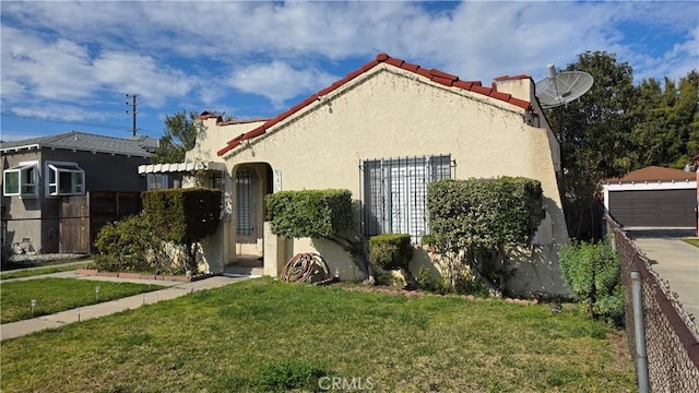 mediterranean / spanish-style house with fence, a detached garage, a front lawn, and stucco siding