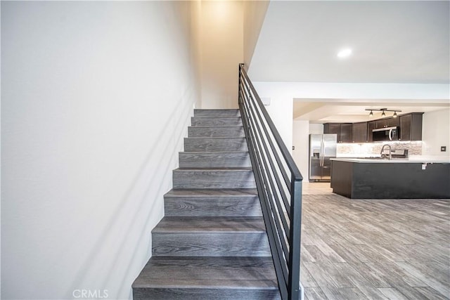 staircase featuring wood finished floors and rail lighting