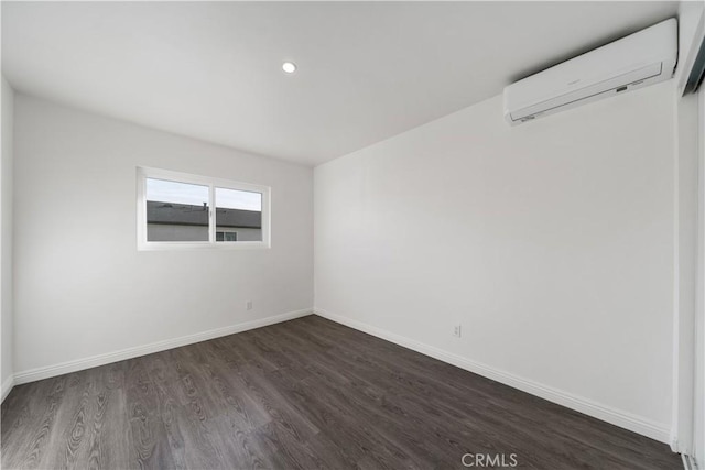 spare room with baseboards, dark wood-type flooring, an AC wall unit, and recessed lighting