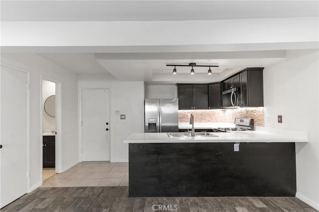 kitchen with a peninsula, a sink, light countertops, appliances with stainless steel finishes, and tasteful backsplash