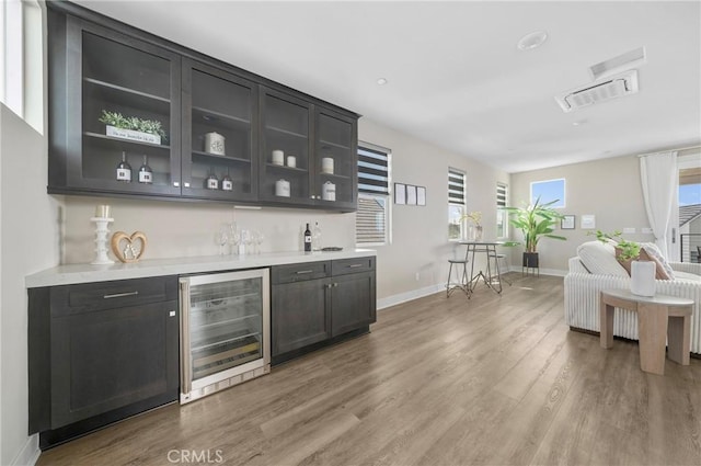 bar with wine cooler, a bar, visible vents, baseboards, and light wood finished floors