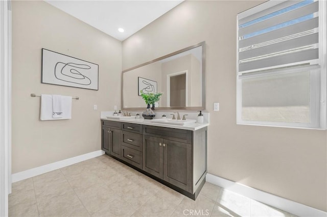 bathroom featuring tile patterned flooring, a sink, baseboards, and double vanity