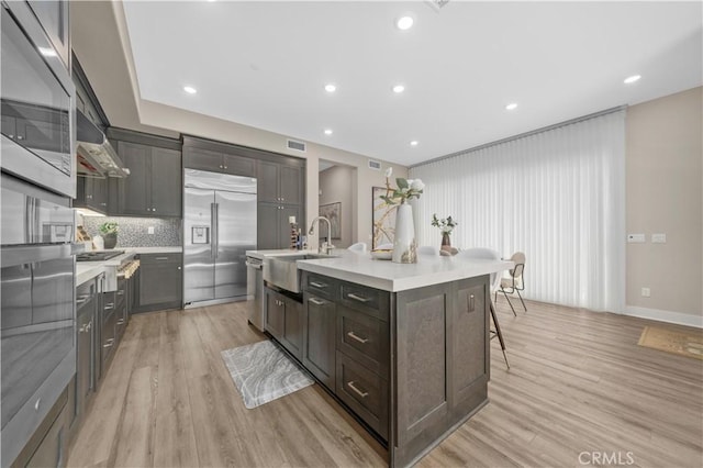 kitchen featuring a breakfast bar, light countertops, light wood-style flooring, appliances with stainless steel finishes, and a sink