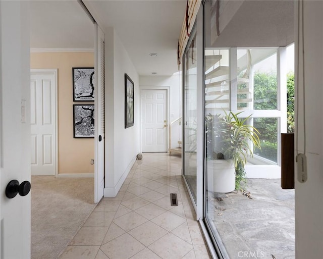hallway featuring baseboards, ornamental molding, light tile patterned flooring, and light colored carpet