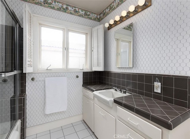 bathroom with tile patterned floors, bath / shower combo with glass door, vanity, and wallpapered walls