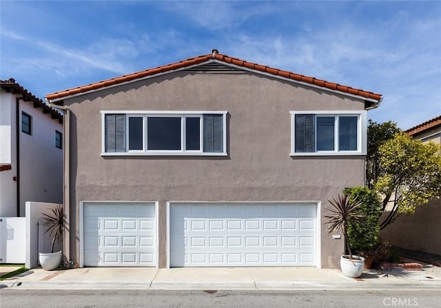 view of side of property featuring driveway, an attached garage, a tiled roof, and stucco siding