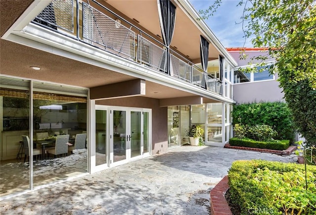 back of house with a balcony, a patio area, and stucco siding