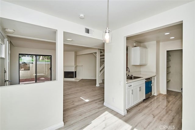 kitchen with hanging light fixtures, dishwasher, light wood-type flooring, sink, and white cabinetry