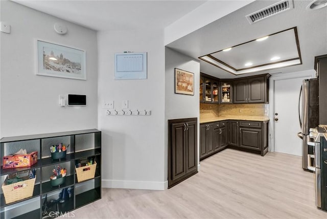 bar with a tray ceiling, light wood finished floors, visible vents, backsplash, and freestanding refrigerator