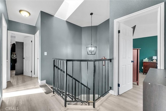 hall with light wood-type flooring, baseboards, a notable chandelier, and an upstairs landing