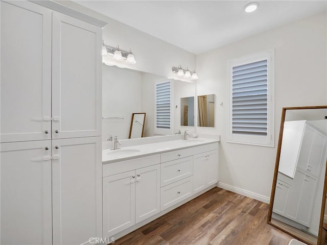 full bathroom with double vanity, baseboards, a sink, and wood finished floors