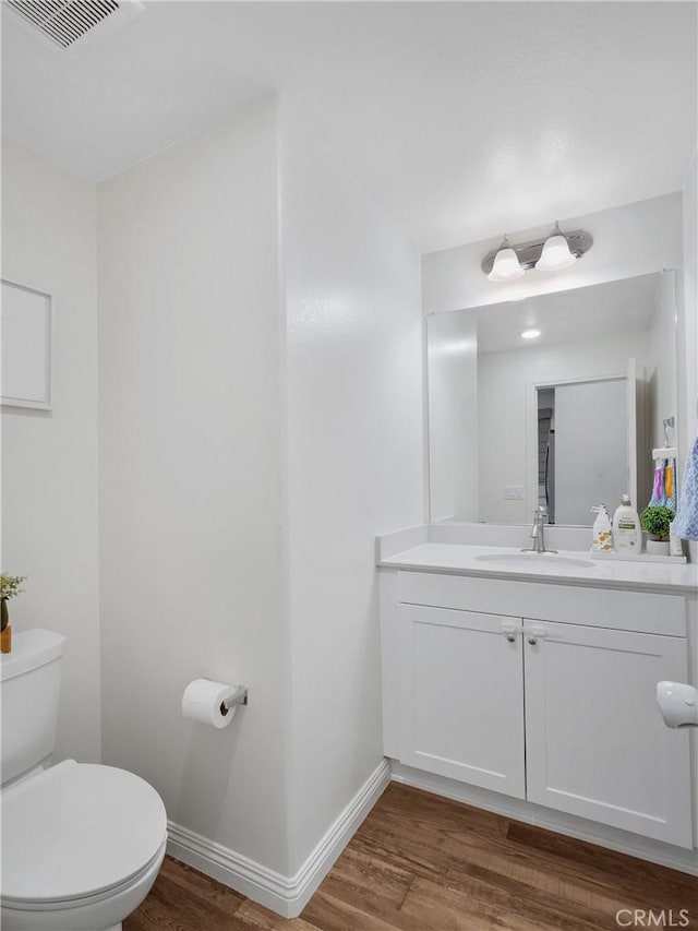 half bath featuring baseboards, vanity, toilet, and wood finished floors