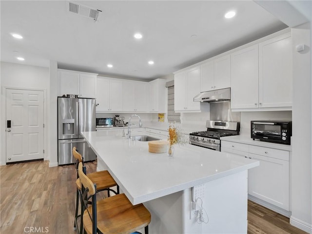 kitchen with stainless steel appliances, white cabinets, a sink, under cabinet range hood, and a kitchen bar