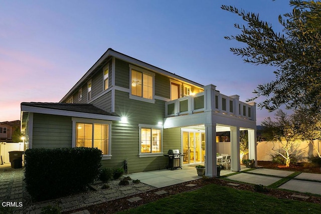 back of house at dusk featuring a patio, fence, and a balcony