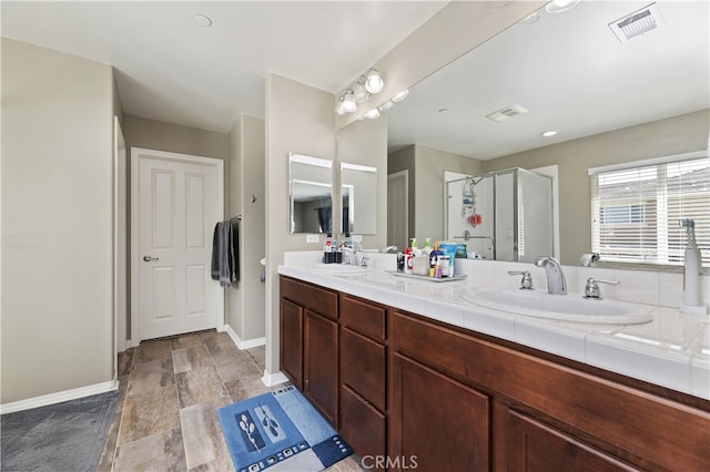 full bathroom with double vanity, baseboards, visible vents, a shower stall, and a sink