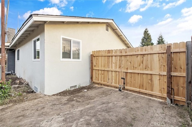 view of property exterior with crawl space, stucco siding, and fence