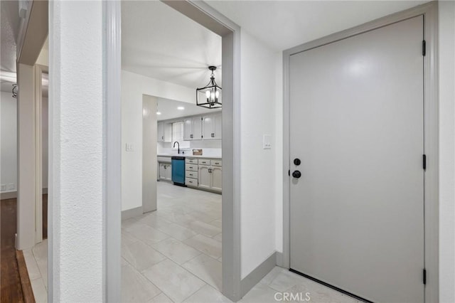 hallway featuring baseboards, a notable chandelier, and a sink