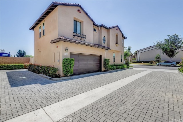 mediterranean / spanish house featuring fence, decorative driveway, a tile roof, and stucco siding