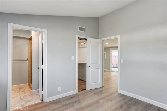 unfurnished bedroom with a walk in closet, lofted ceiling, a closet, visible vents, and baseboards