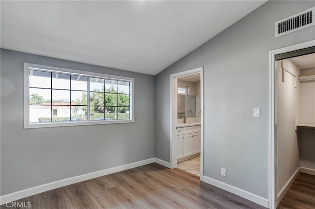 unfurnished bedroom with lofted ceiling, light wood-style flooring, visible vents, and baseboards