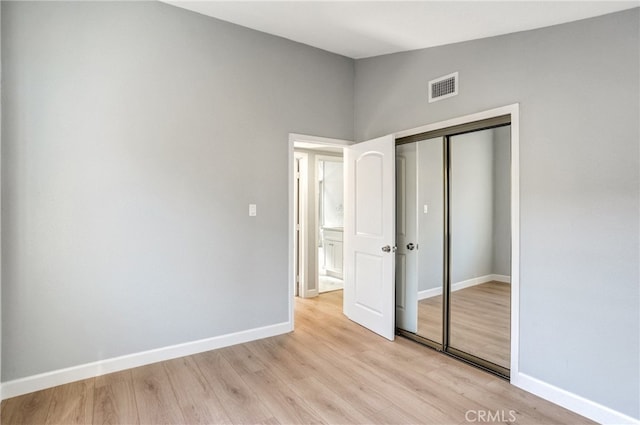 unfurnished bedroom featuring baseboards, a closet, visible vents, and light wood-style floors