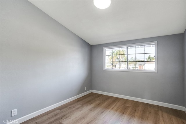 empty room with lofted ceiling, light wood finished floors, and baseboards