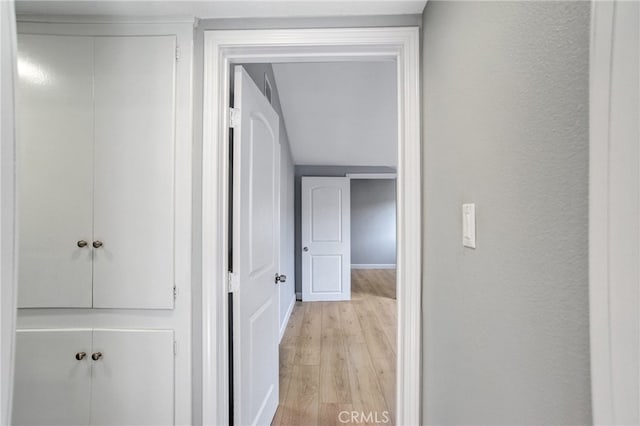 hallway featuring light wood-style floors, baseboards, and a textured wall