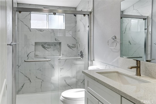 bathroom featuring toilet, a marble finish shower, and vanity