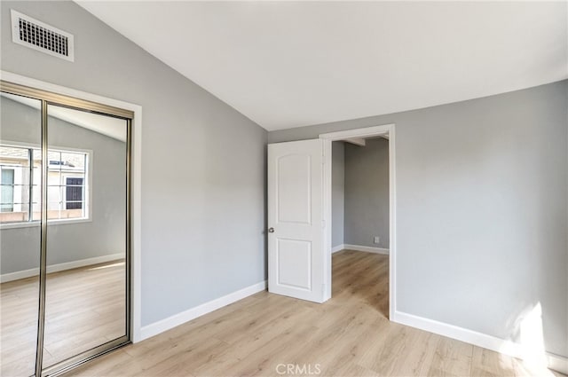 unfurnished bedroom featuring light wood finished floors, a closet, visible vents, vaulted ceiling, and baseboards