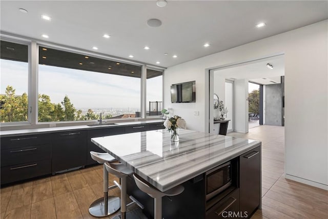 kitchen featuring a kitchen island, built in microwave, dark cabinetry, light countertops, and a kitchen breakfast bar