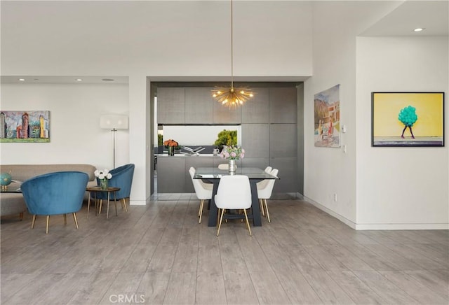 dining space with light wood-type flooring, baseboards, recessed lighting, a high ceiling, and an inviting chandelier