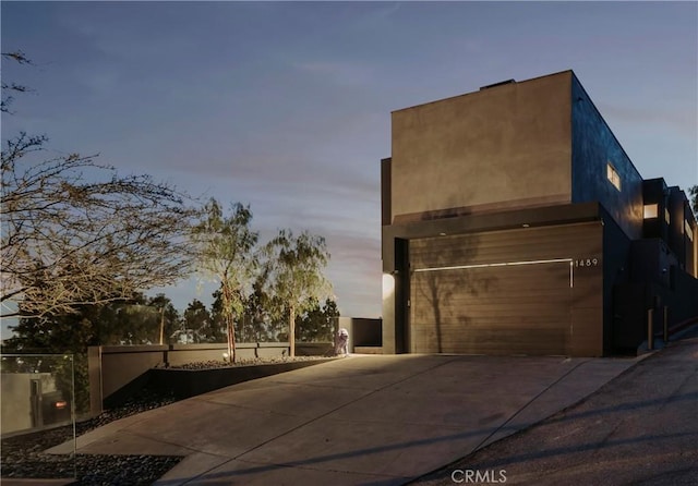 exterior space with concrete driveway, an attached garage, fence, and stucco siding