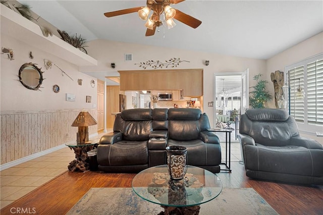 living room with lofted ceiling, wood finished floors, visible vents, a wainscoted wall, and a ceiling fan