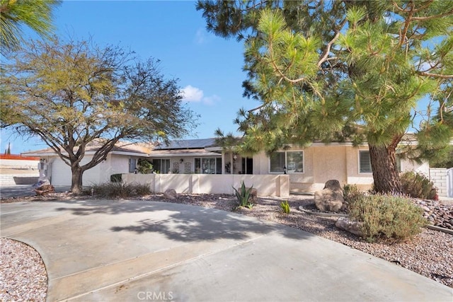 view of front of property featuring stucco siding, fence, roof mounted solar panels, an attached garage, and driveway