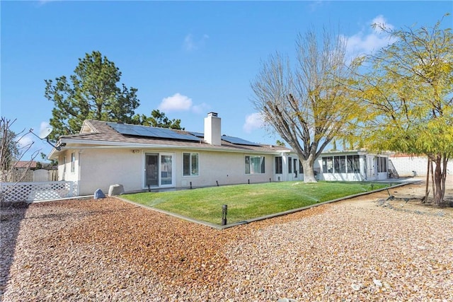 rear view of property with stucco siding, fence, a lawn, solar panels, and a chimney