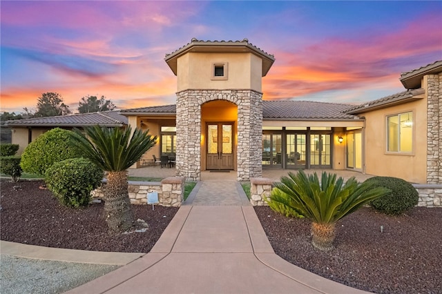 exterior entry at dusk featuring french doors, a tile roof, a patio, and stucco siding