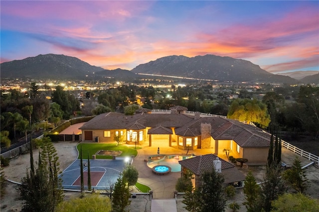 back of house at dusk with a mountain view, a tiled roof, and fence