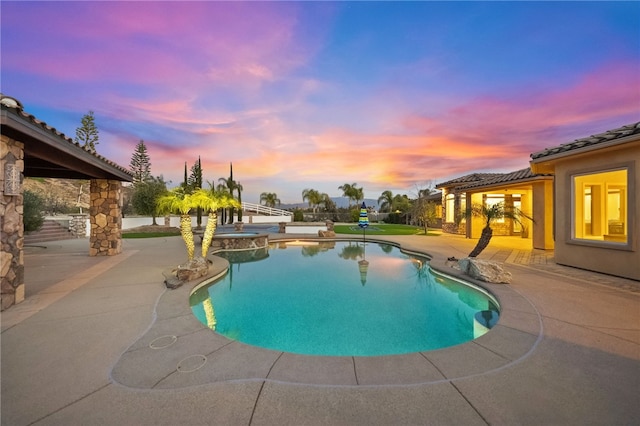 pool at dusk featuring a patio area and a pool with connected hot tub