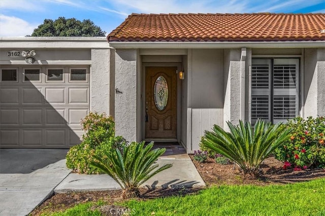 entrance to property featuring a garage, a tile roof, and stucco siding