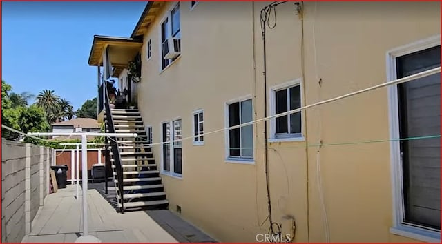 view of side of home with fence, stucco siding, and stairs