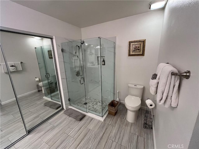 bathroom with wood tiled floor, a marble finish shower, baseboards, and toilet