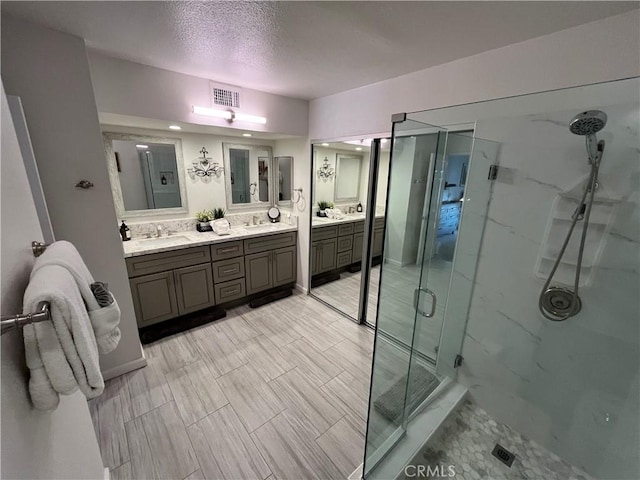 full bathroom with double vanity, a marble finish shower, visible vents, and a sink