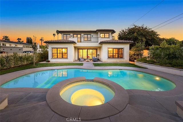 rear view of property featuring a balcony, a pool with connected hot tub, a tiled roof, stucco siding, and a patio area