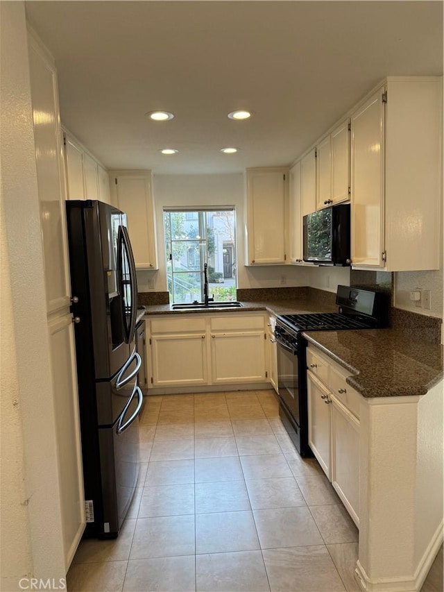 kitchen featuring light tile patterned floors, a sink, white cabinets, dark stone counters, and black appliances