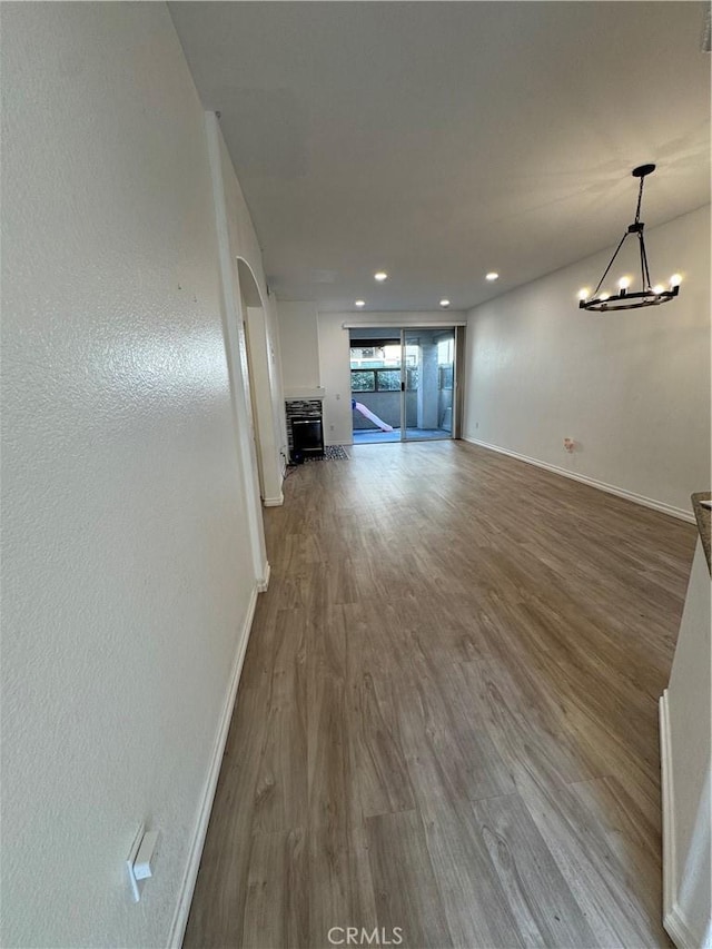 unfurnished living room featuring wood finished floors, baseboards, an inviting chandelier, recessed lighting, and arched walkways