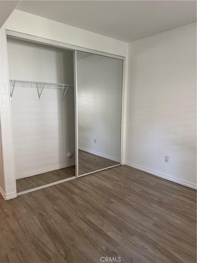 unfurnished bedroom with dark wood-type flooring, a closet, and baseboards