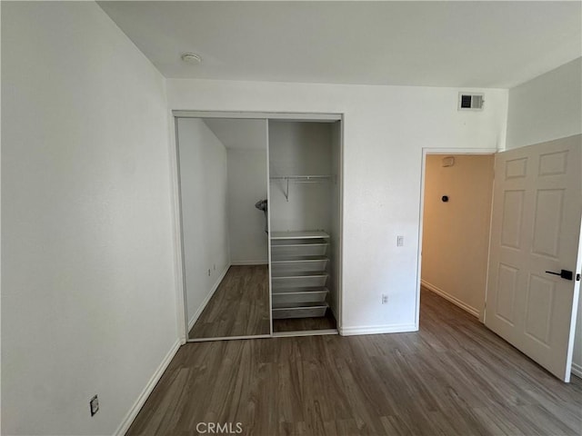 unfurnished bedroom featuring wood finished floors, visible vents, a closet, and baseboards