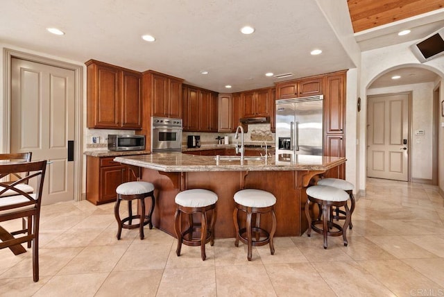 kitchen featuring a sink, a kitchen island with sink, arched walkways, and stainless steel appliances