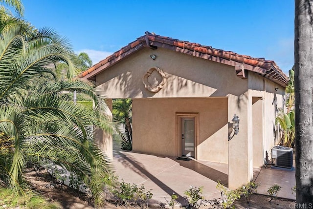 exterior space with a tiled roof, central air condition unit, stucco siding, and a patio